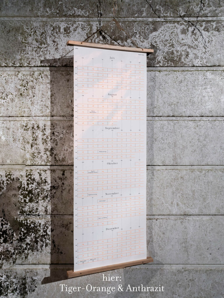 Tiger-Orange & Anthrazit Siebdruck-Wandkalender hängt vor einer Betonwand